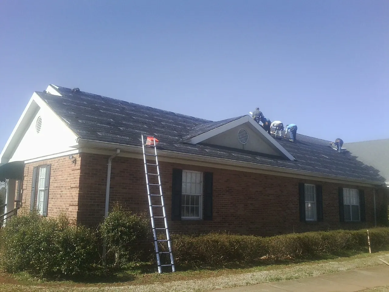 Crew tearing shingles off a brick ranch roof with a ladder set — Metal Roof Repair work by our crew in Macedonia
