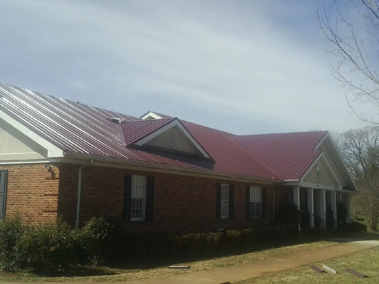 Red metal roof with gabled entries on a long brick building, from a Hail Damage Roof Repair job in Macedonia